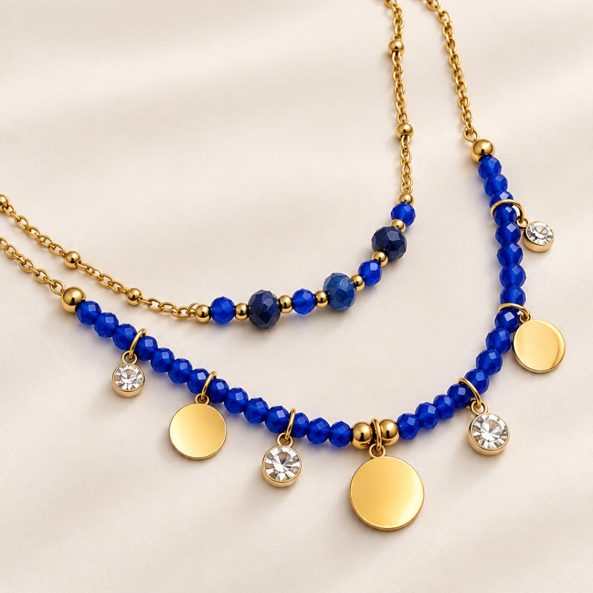 Collier double Cassandre en acier inoxydable doré à l'or fin 24K avec perles bleues et zircons, vu en gros plan sur fond clair